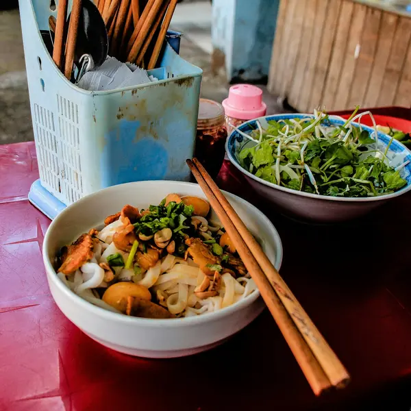 A street-food breakfast in Da Nang: noodles, herbs and chopsticks on a red plastic table