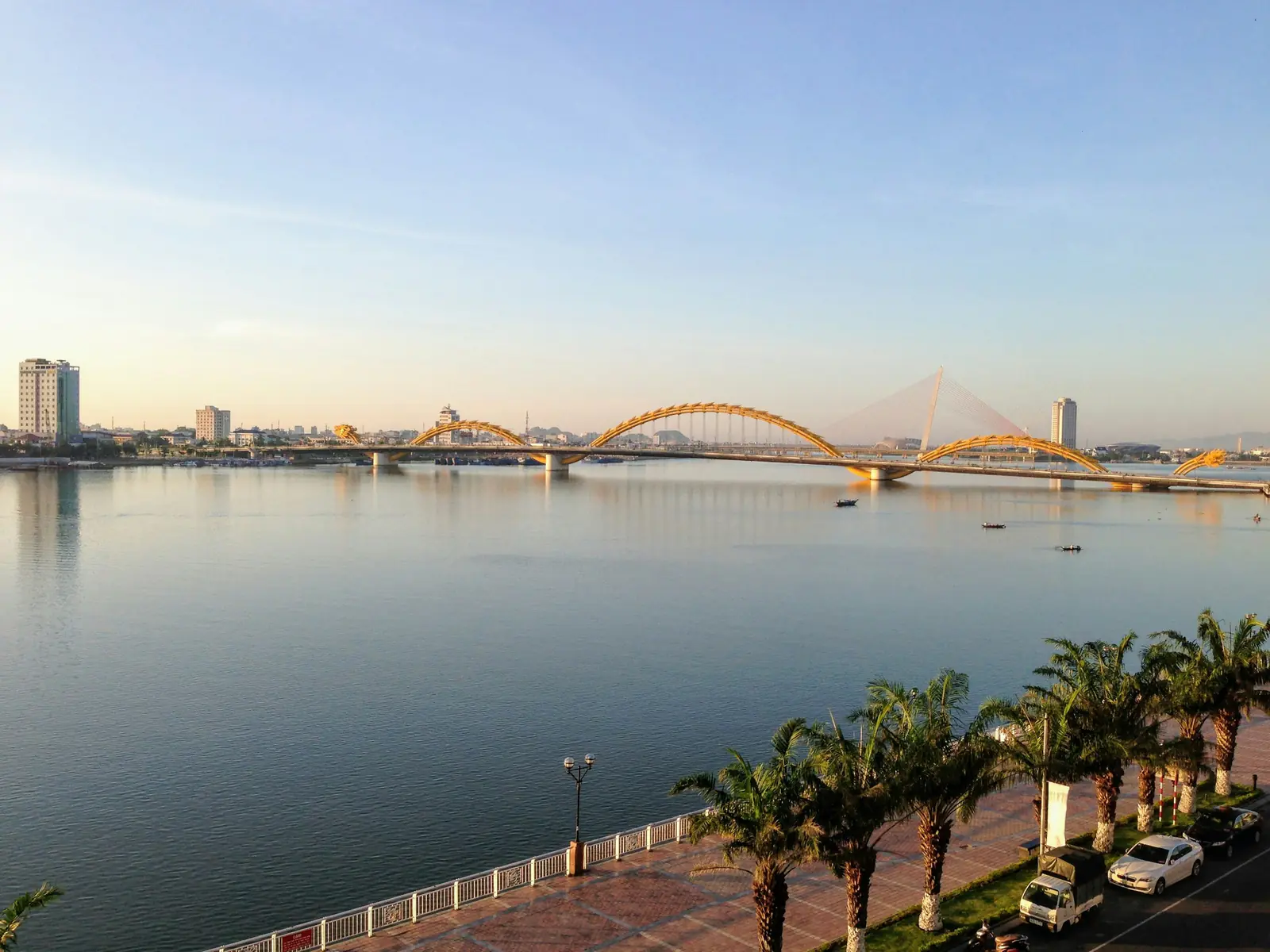The Han River at golden hour, calm as glass, with the Dragon Bridge arching across it and palms along the promenade